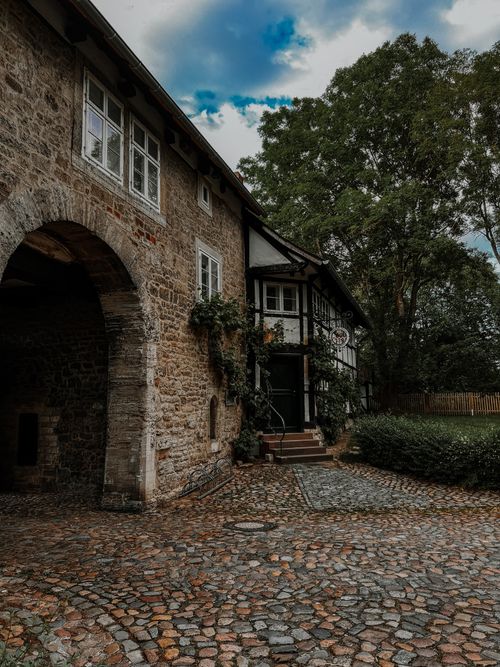 Free Historic stone cottage with arches and cobblestone pathway in a lush green setting. Stock Photo