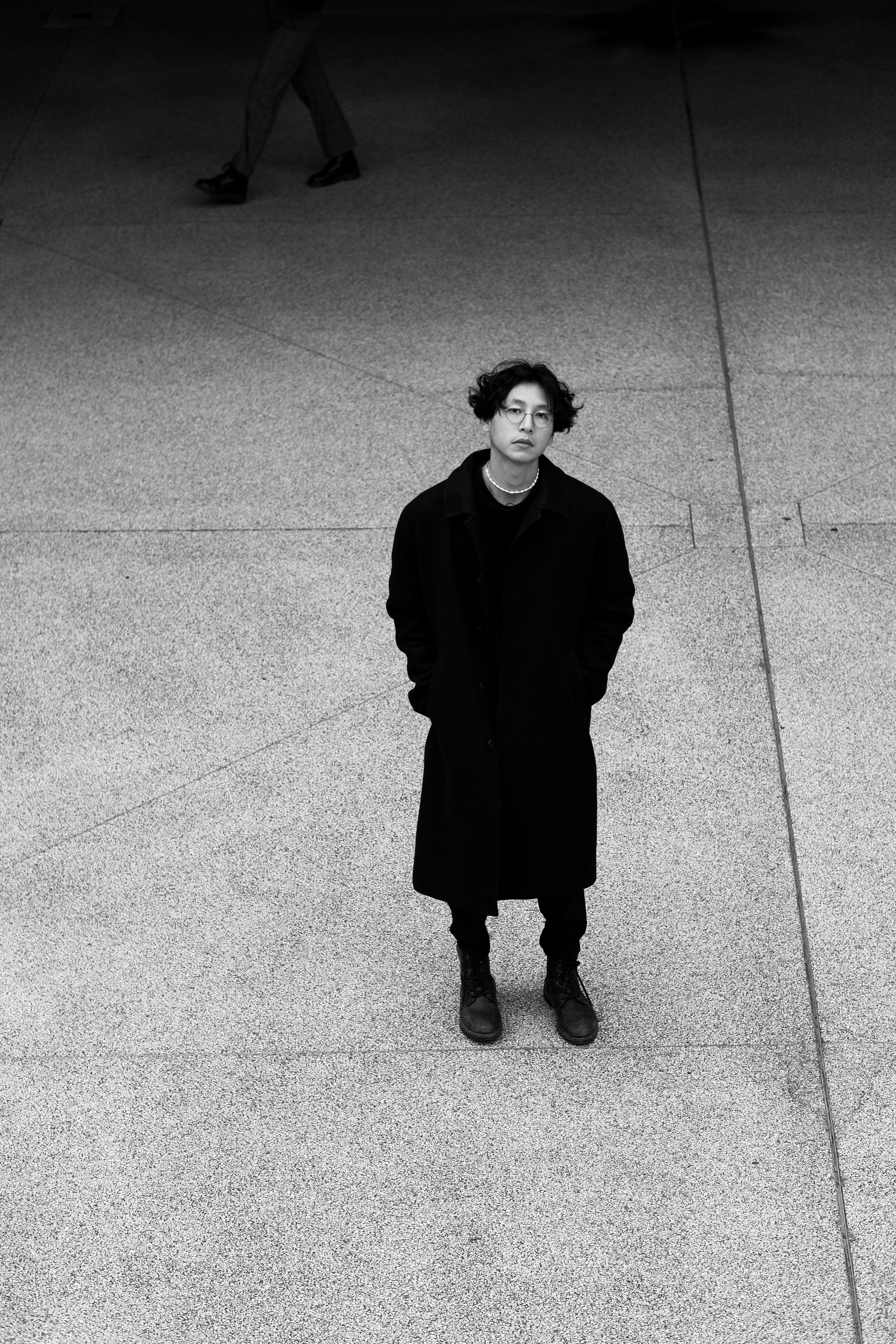 Black and white photo of a person in a black coat standing in Berlin's urban environment.