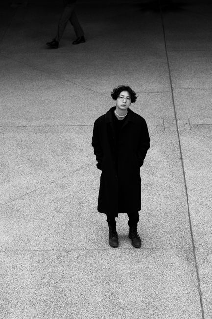 Black and white photo of a person in a black coat standing in Berlin's urban environment.