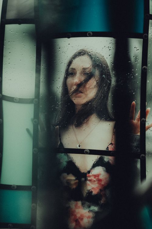 Free Moody portrait of a woman in a floral dress behind a rain-streaked window, capturing emotion. Stock Photo