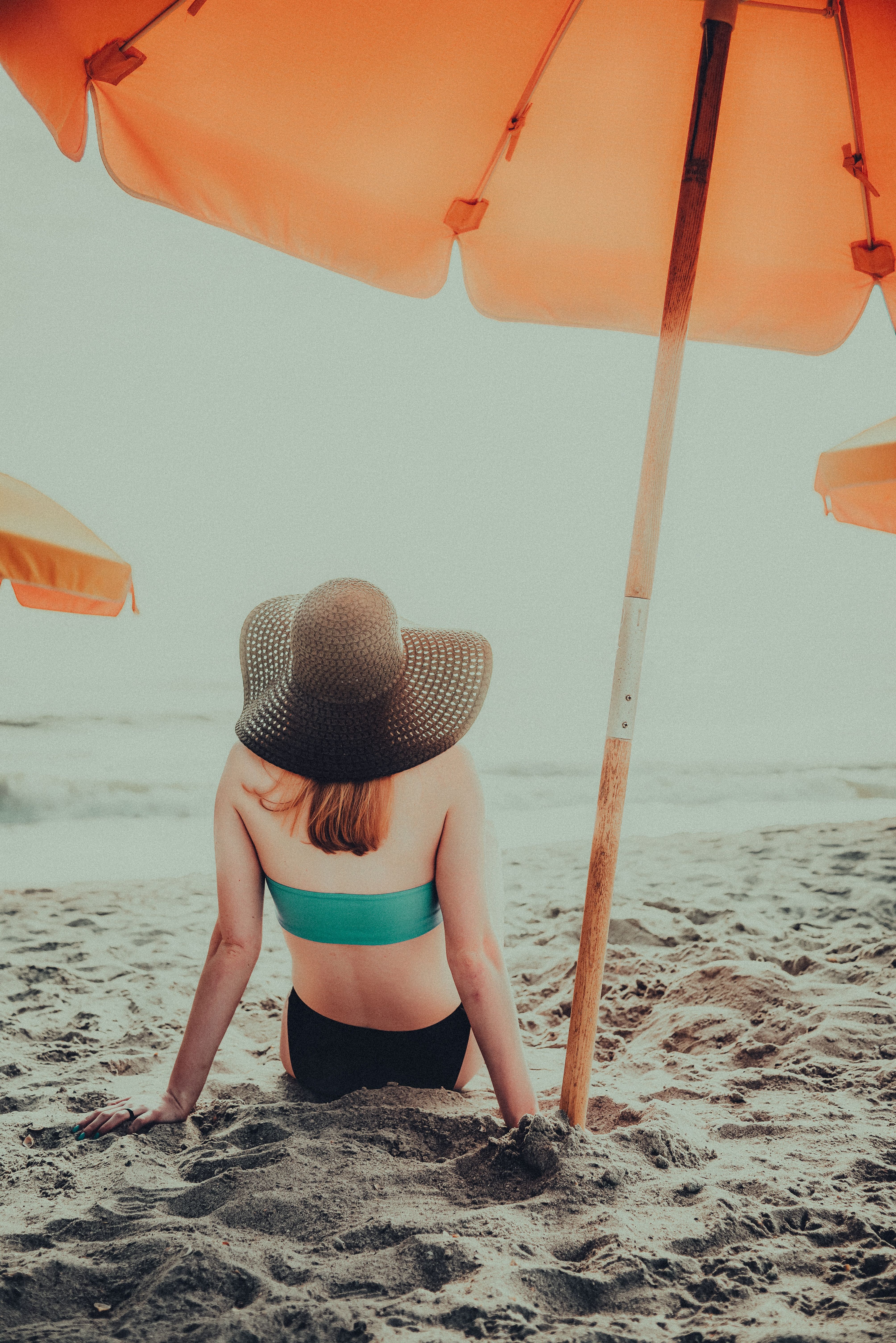 Woman sitting under a beach umbrella, enjoying a sunny day by the sea.