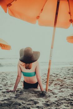 Woman sitting under a beach umbrella, enjoying a sunny day by the sea.
