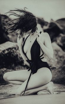 Striking black and white photo of a woman kneeling on a beach in a swimsuit.