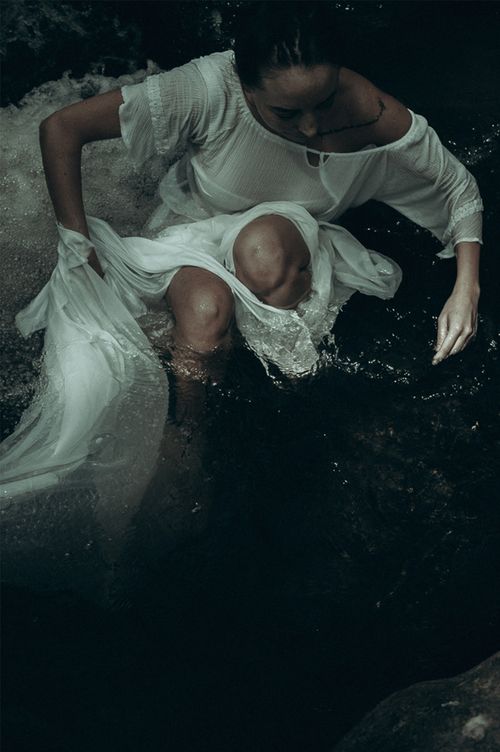 Free A woman in a white dress sits in a river at night, creating a mysterious and serene atmosphere. Stock Photo