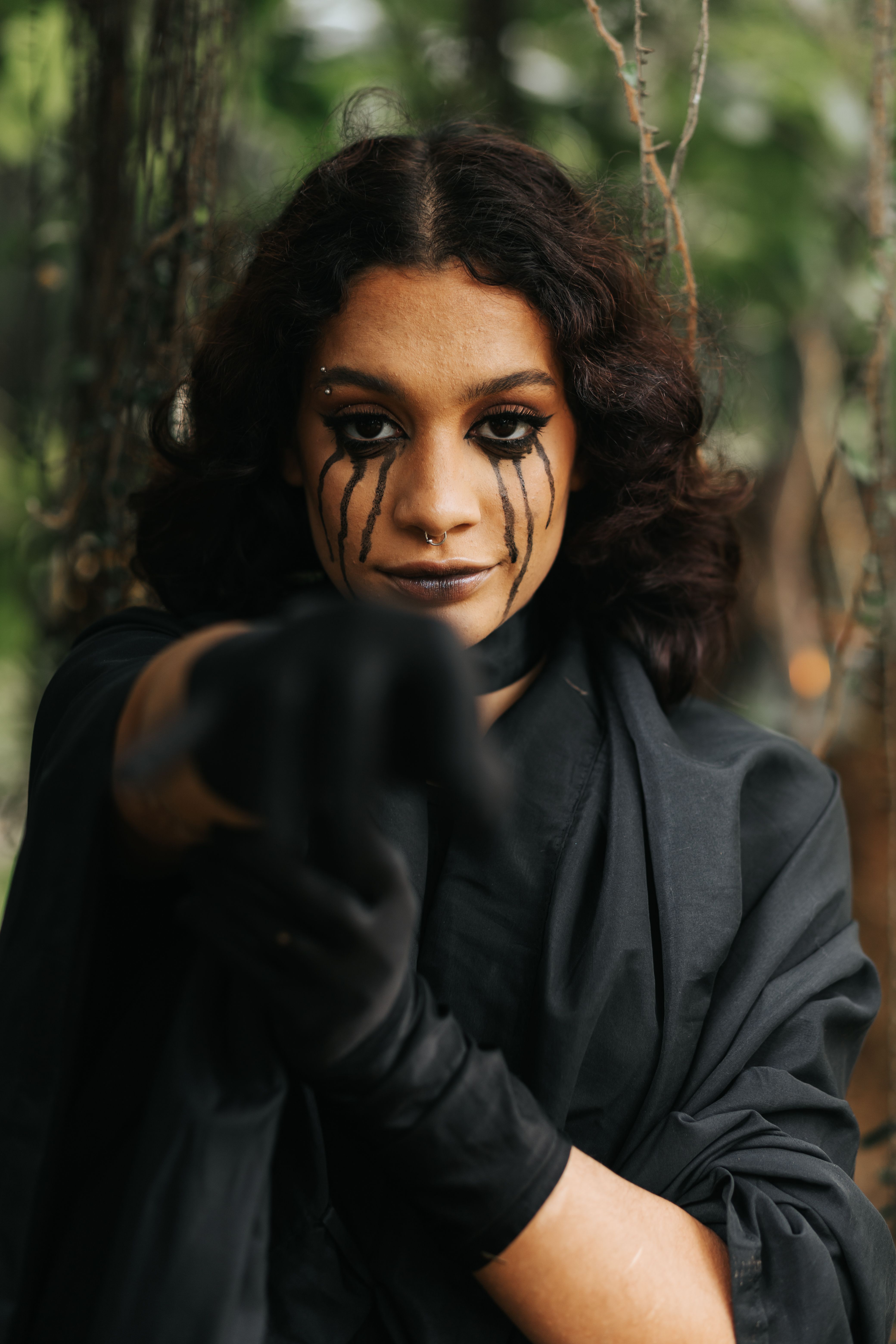 Portrait of a woman with gothic makeup pointing, surrounded by nature, filling the atmosphere with mystique.