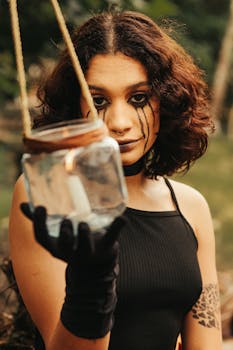 Woman with dramatic makeup holding a jar containing a candle, evoking mystery and fantasy.