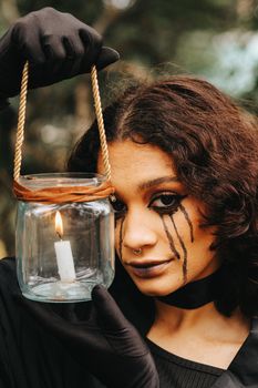 A woman with dramatic makeup holds a glowing candle lantern, creating a spooky Halloween atmosphere.