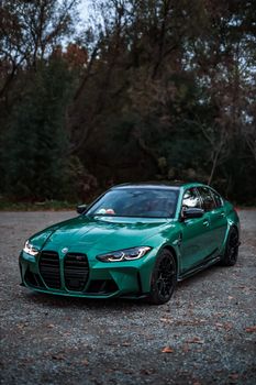 A luxury green sports car parked on gravel with autumn foliage background.