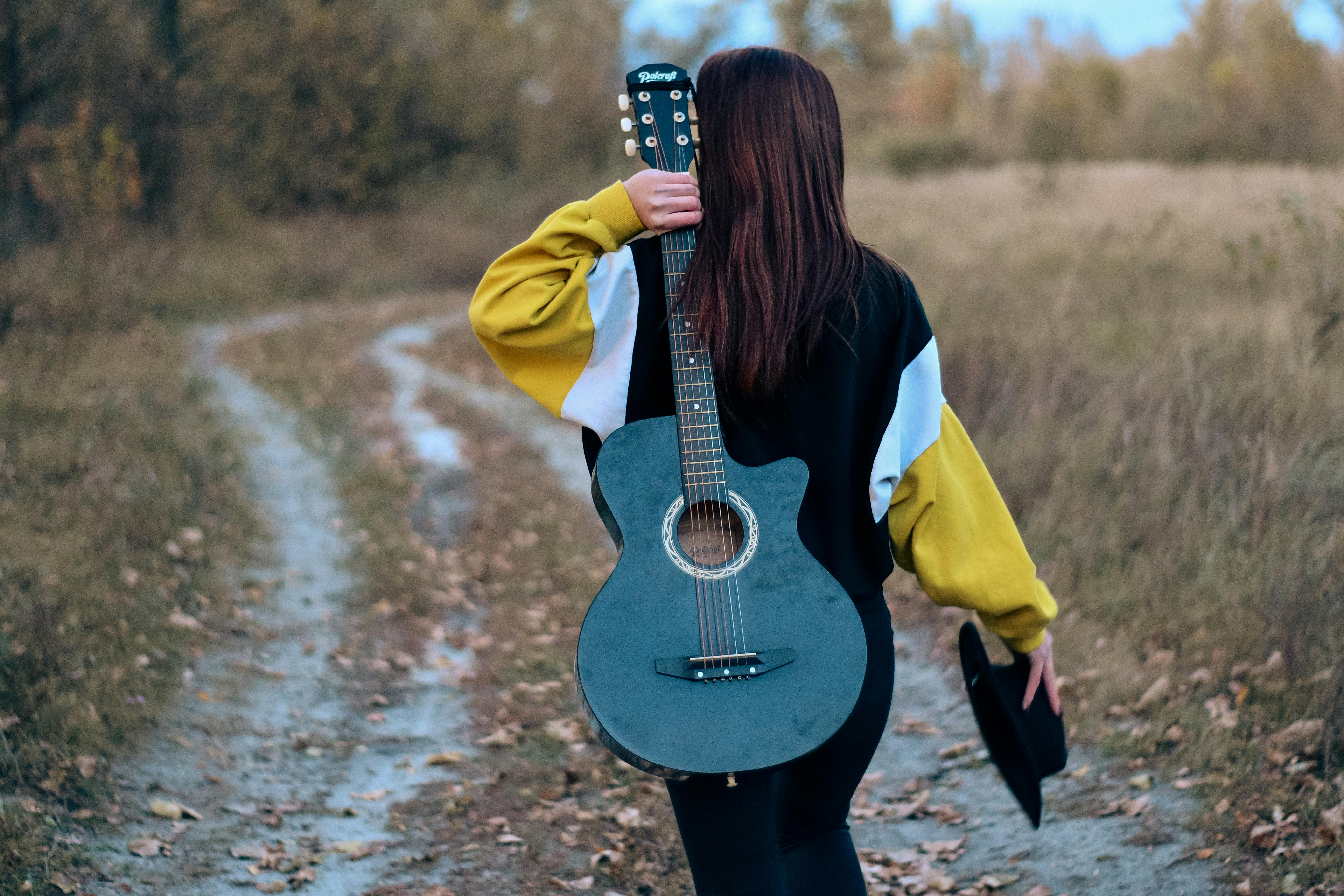 Woman Walking down the Country Road with a Guitar on her Back