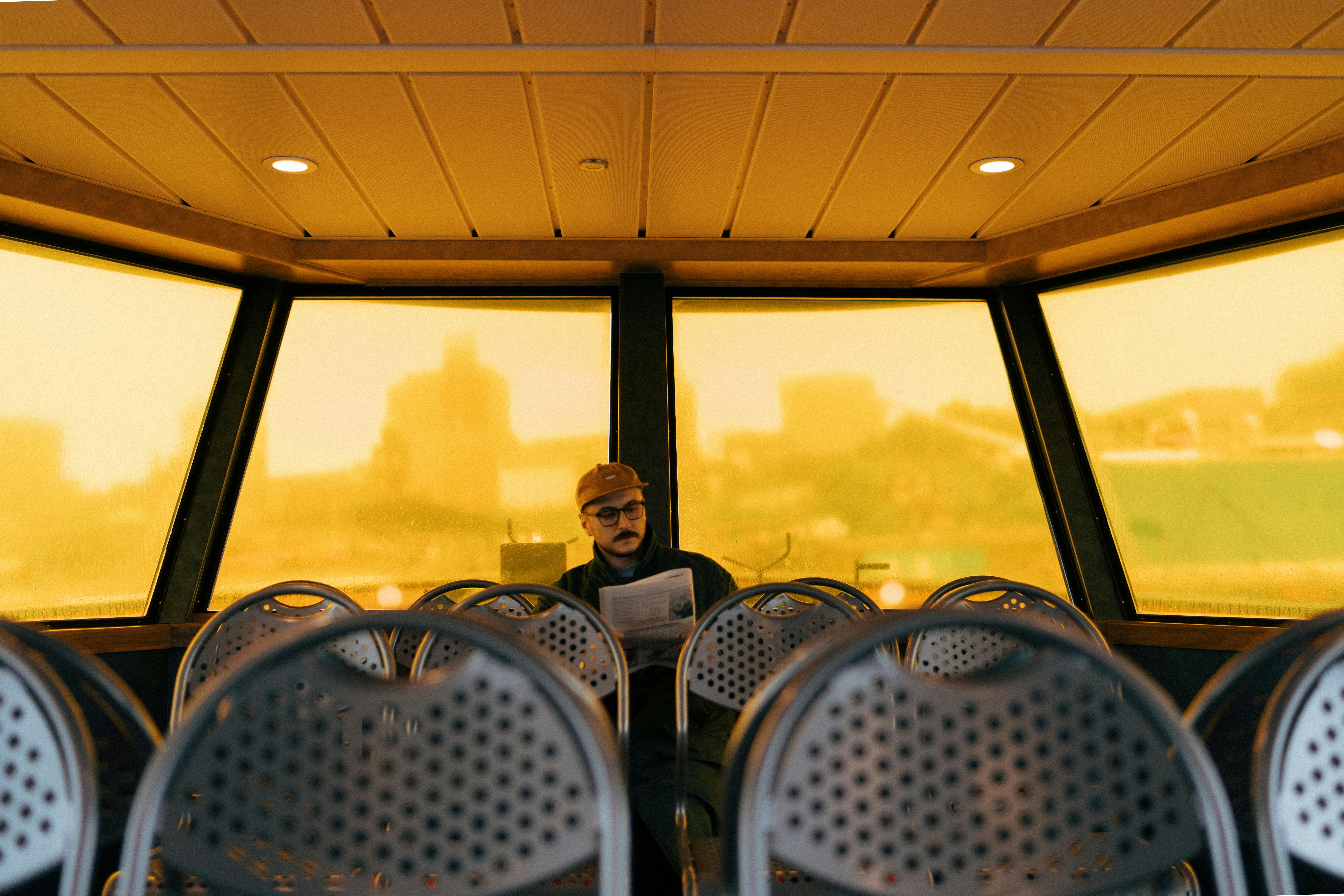 A man reads a newspaper inside a ferry with empty chairs, offering a calm urban transportation scene.