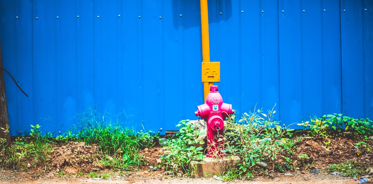 Free Pink Steel Water Pump Behind Blue Fence Stock Photo