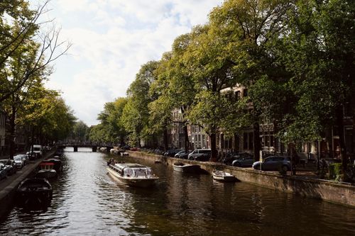 Free Idyllic view of Amsterdam's canal with boats and lush greenery on a sunny day. Stock Photo