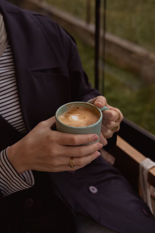 Free A woman holding a frothy cup of coffee indoors, conveying warmth and relaxation. Stock Photo