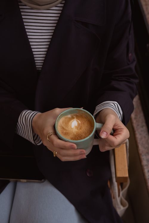 Free Close-up of a woman holding a latte with froth art indoors, creating a cozy ambiance. Stock Photo
