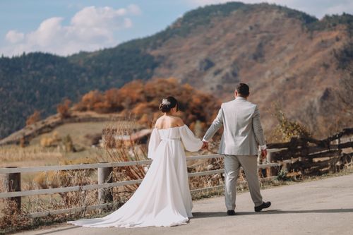 Free Bride and groom walking hand in hand along a scenic mountain road, capturing a timeless wedding moment. Stock Photo