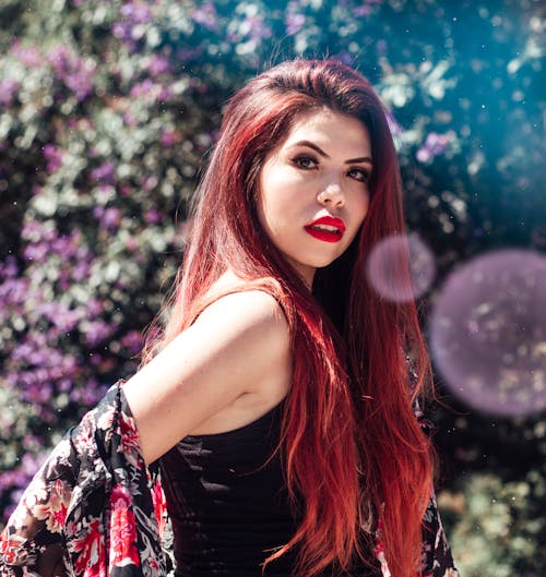 Femme Aux Cheveux Rouges En Débardeur Noir Debout Près De La Plante Verte à Fleurs Violettes