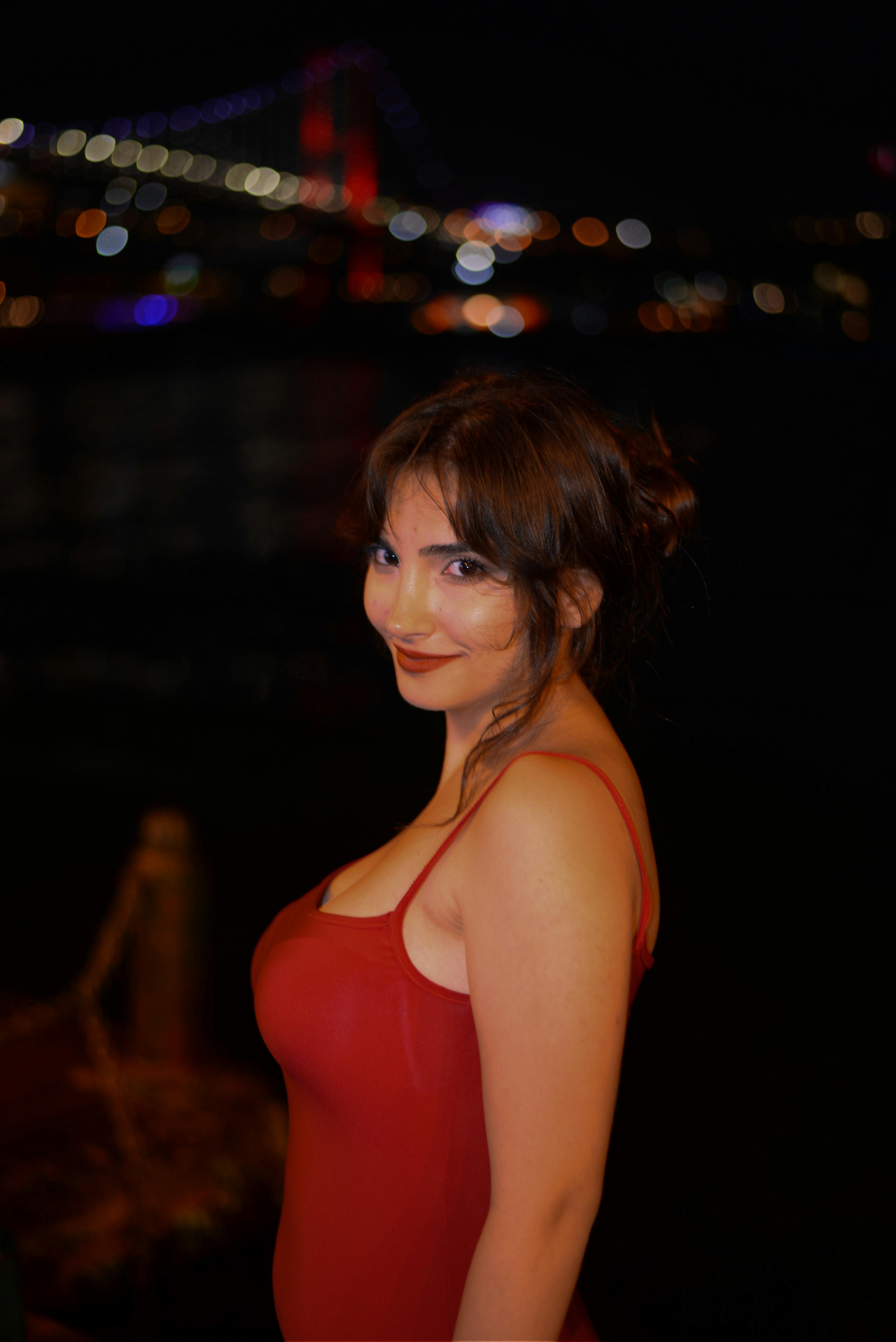 Portrait of a woman in a red dress posing at night with city lights in the background, exuding elegance.