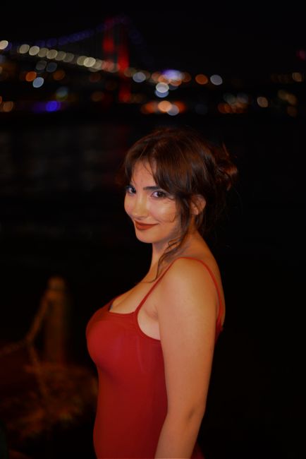 Portrait of a woman in a red dress posing at night with city lights in the background, exuding elegance.