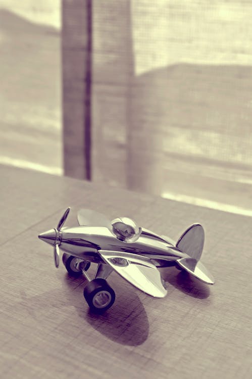 Free Sepia Photography of Stainless Steel Biplane on Brown Wooden Table Near Window during Daytime Stock Photo