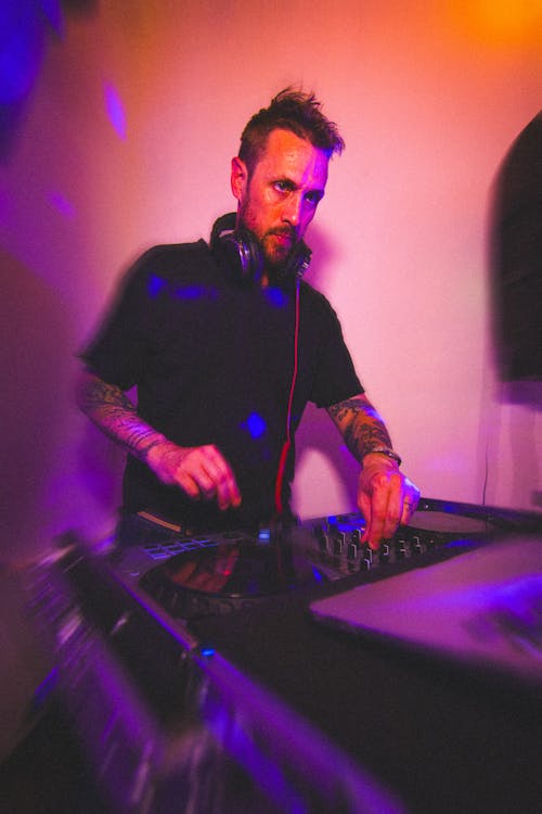 Man with Tattoos Standing behind the Console and Mixing Music 