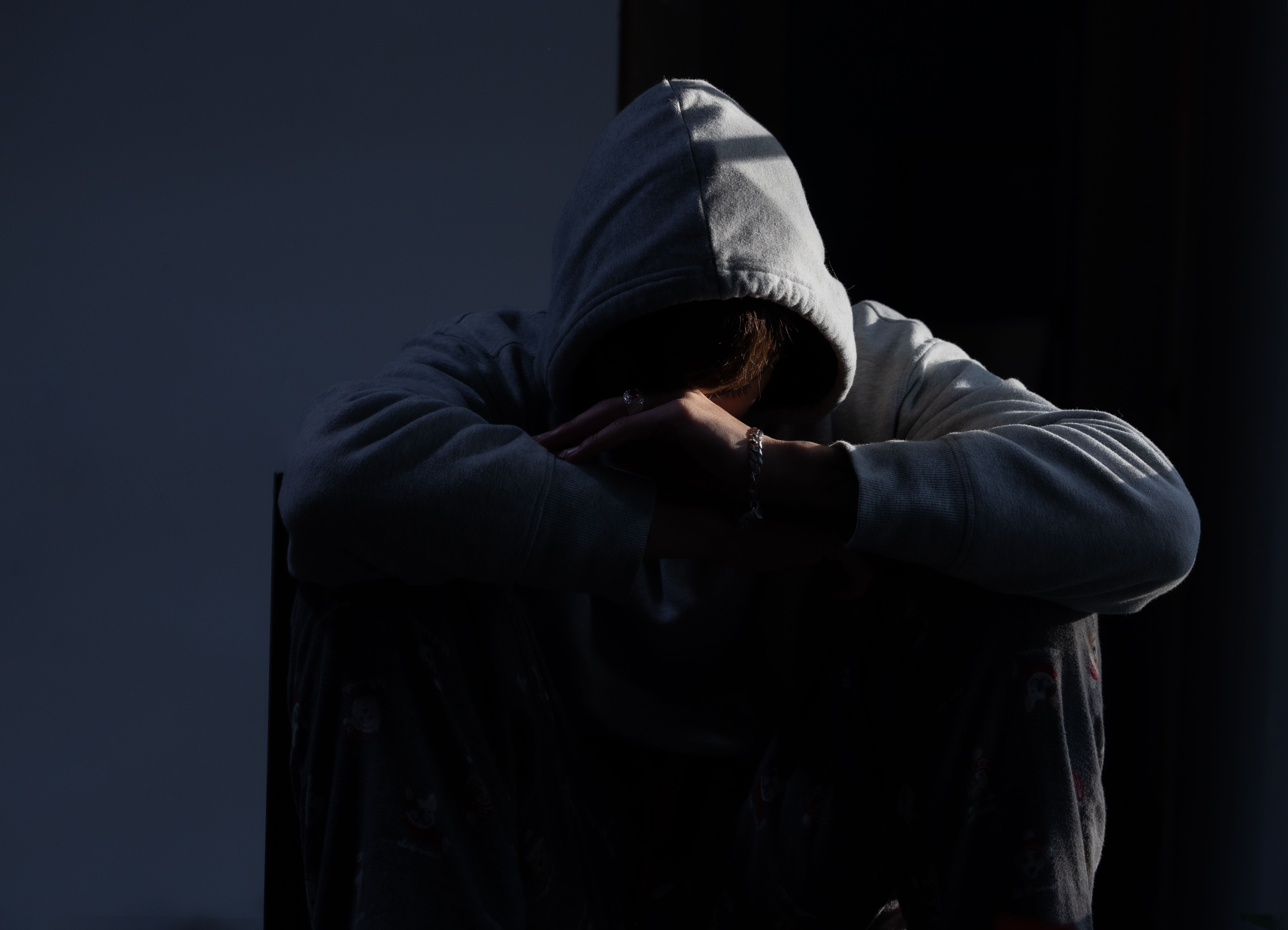 Young person in hoodie sitting alone in shadows — the quiet aftermath of a blown trading account