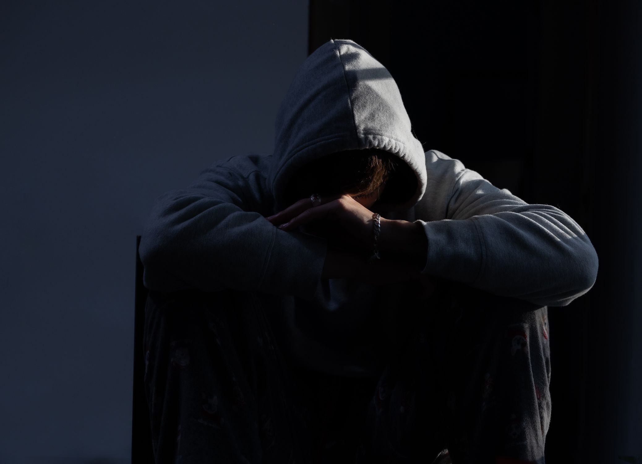 Young person in hoodie sitting alone in shadows — the quiet aftermath of a blown trading account