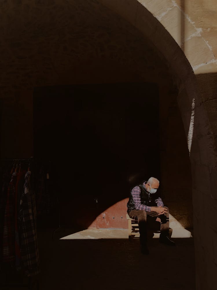 Elderly Man Sitting By Wall In Shadow