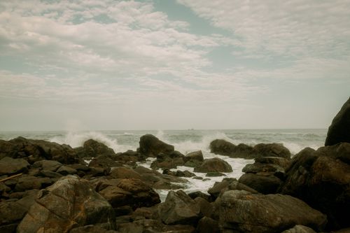 Free Capture of a rugged seashore with crashing waves against rocky formations under a cloudy sky. Stock Photo