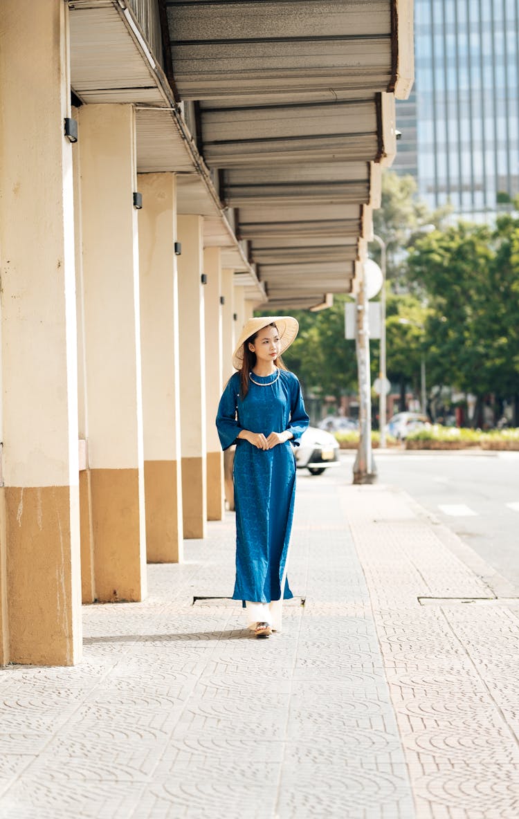 Woman In A Blue Gown And A Conical Hat Walking On The Sidewalk 