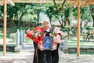 A young Muslim woman celebrating graduation in Shah Alam, Malaysia, outdoors in a park with flowers.