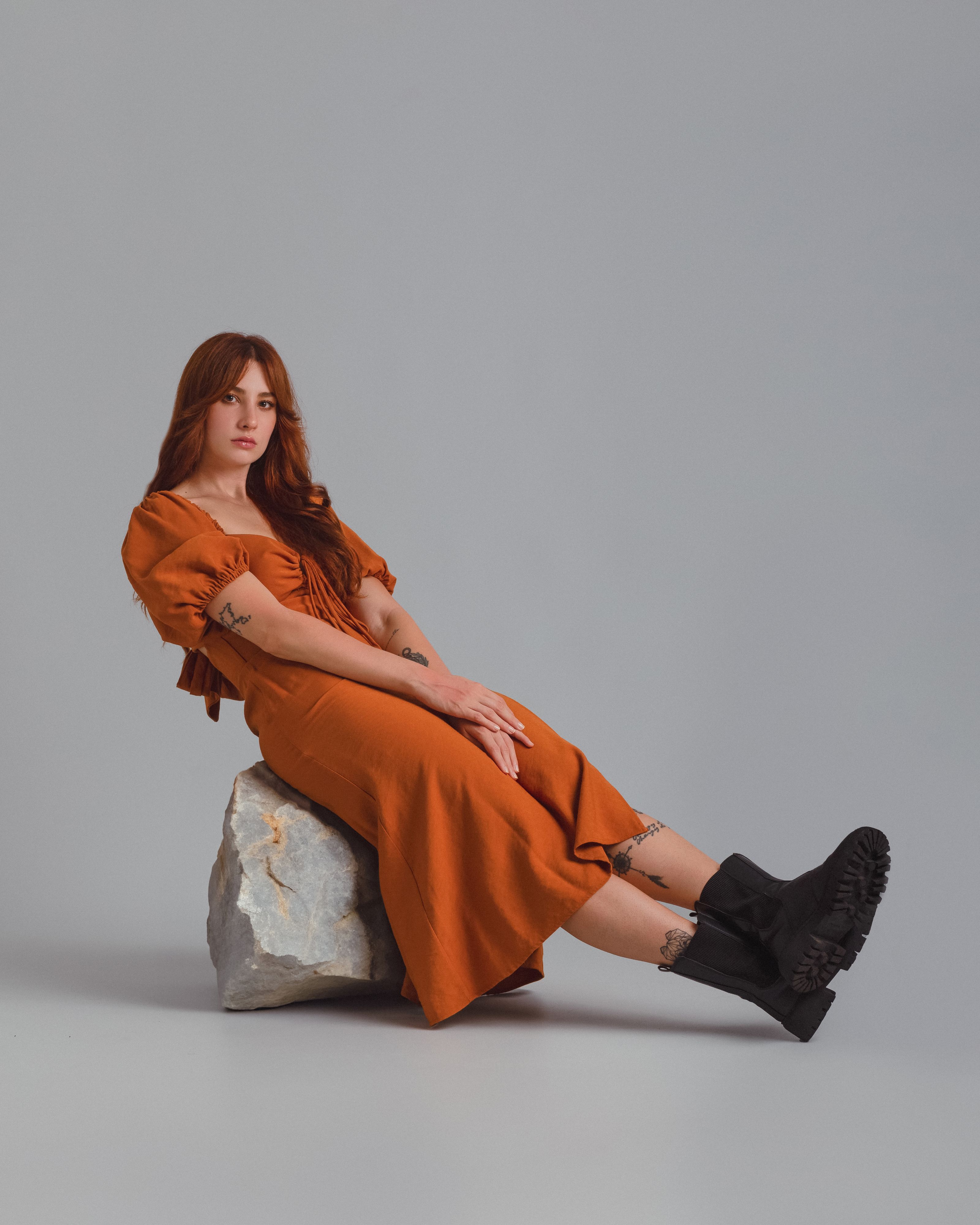 Retrato de moda de uma mulher em um vestido laranja e botas posando internamente sobre uma rocha.