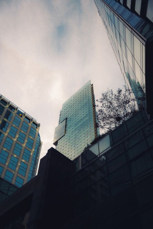 Free Low-angle view of modern skyscrapers with glass facades reflecting a cloudy sky in an urban setting. Stock Photo