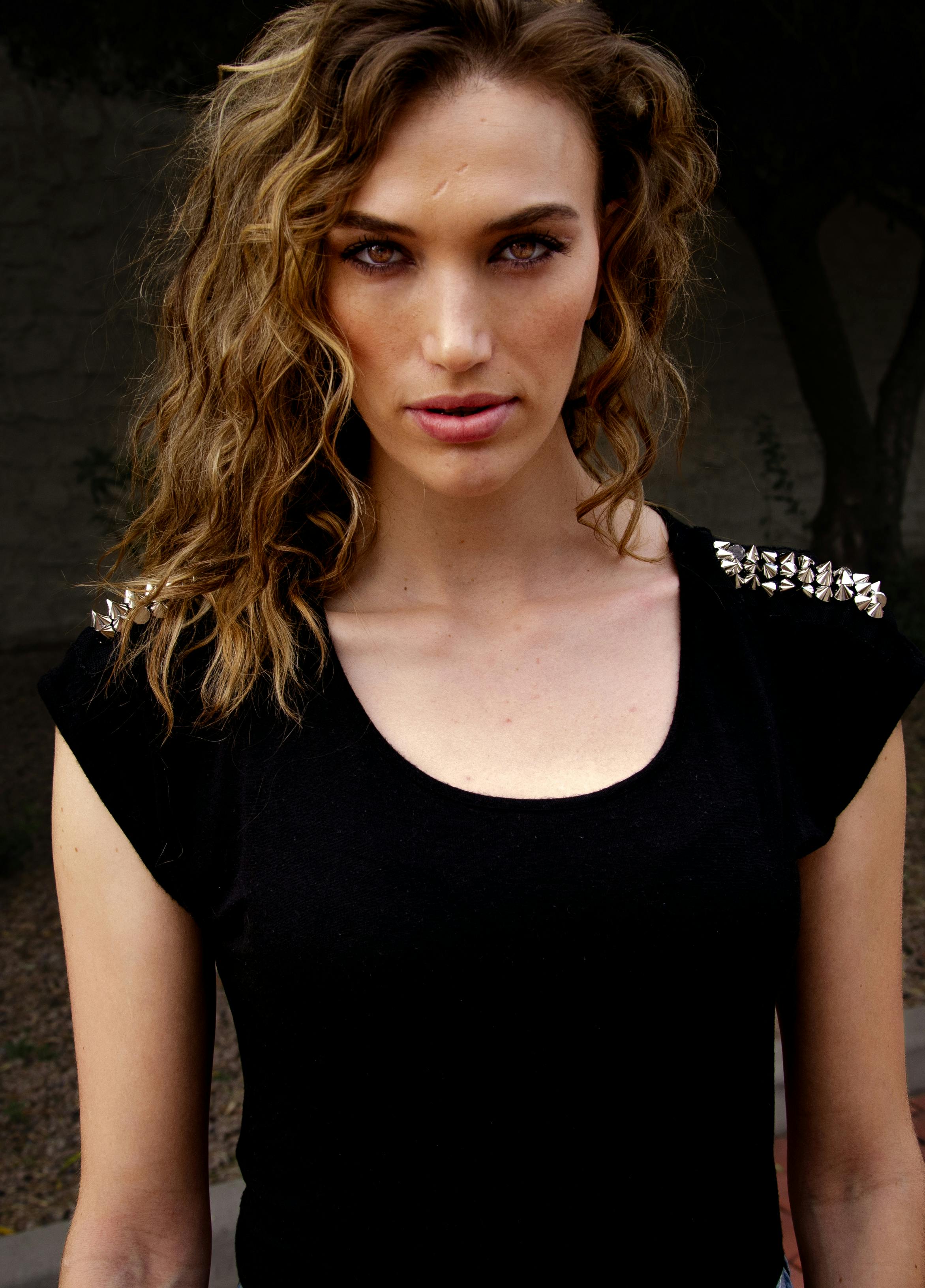 Striking portrait of a woman with curly hair and black attire, showcasing fashion style.
