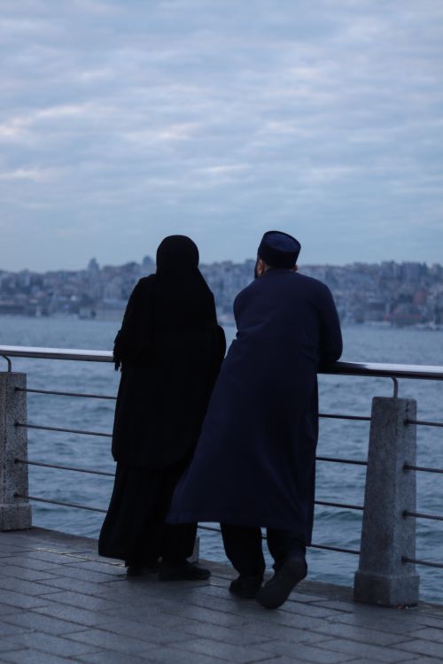 Free Couple enjoying a serene moment by the waterfront bridge during a twilight evening. Stock Photo