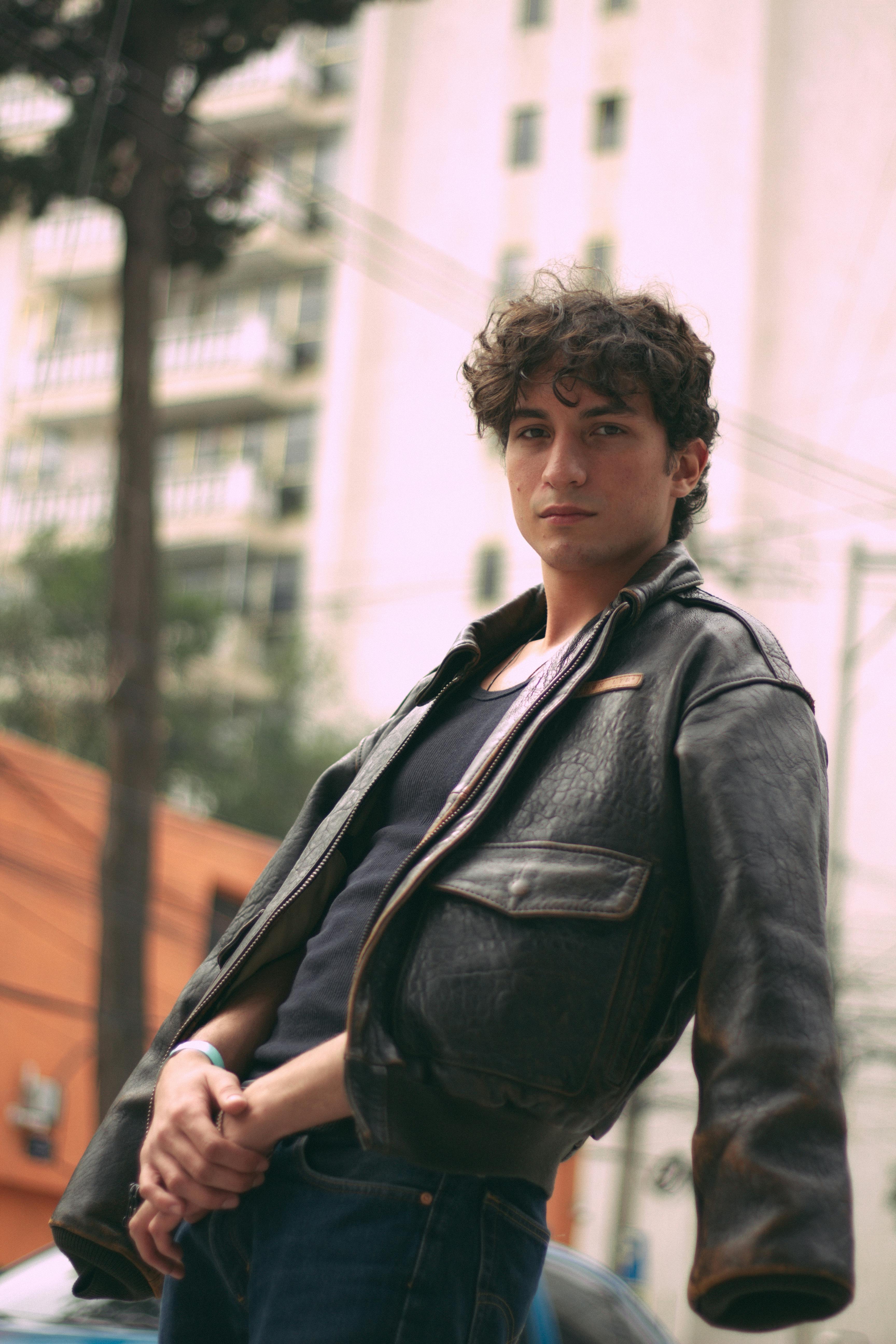 Stylish young man in leather jacket against city backdrop. Urban fashion vibe.