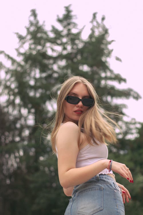Blonde Woman in Black Sunglasses Posing in Beige Tank Top and Blue Jeans