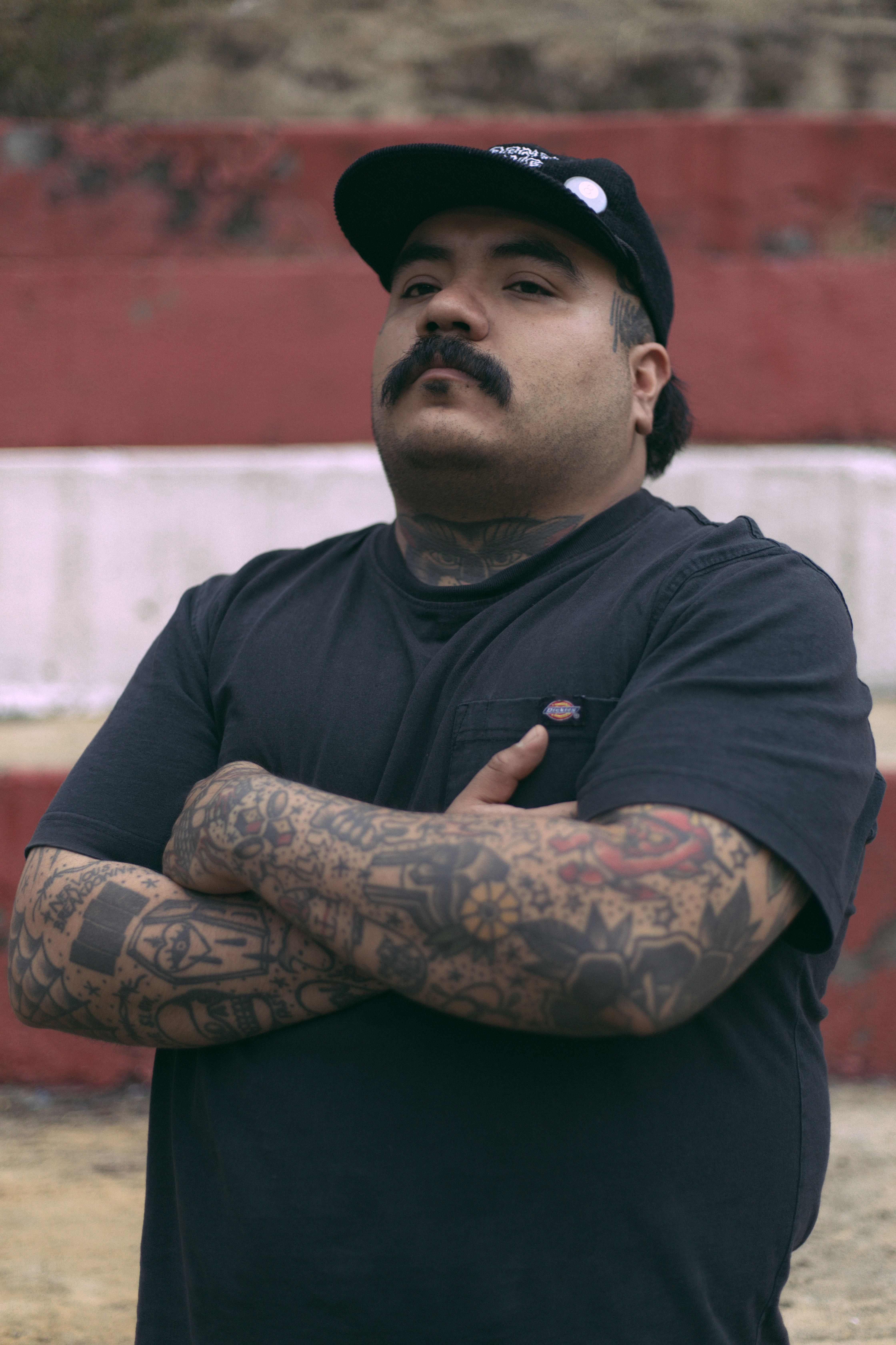 Portrait of a tattooed man with arms crossed, outdoors in casual attire.