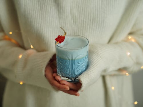 Woman in White Sweater Holding a Glass of Blue Milk Shake Cocktail