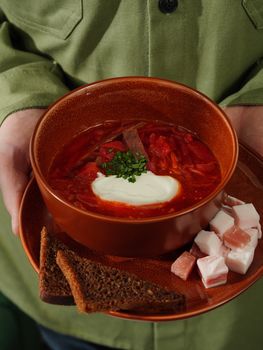 A warm bowl of borscht with sour cream, served with rye bread and meat. Perfect for a comforting meal.