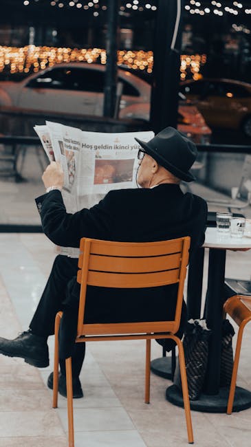 Senior adult male reading a newspaper in a cozy cafe setting, showcasing a moment of relaxation.
