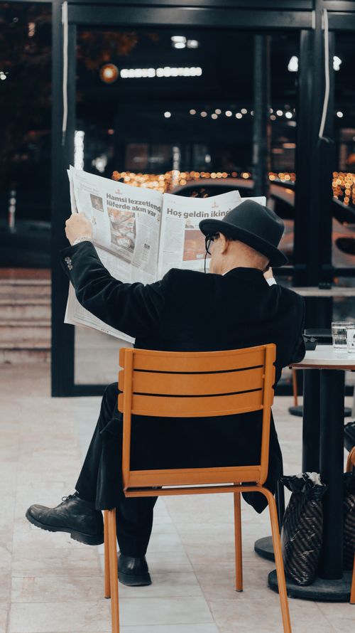 Free A senior adult man reads a newspaper in a contemporary cafe setting, creating a classic urban scene. Stock Photo