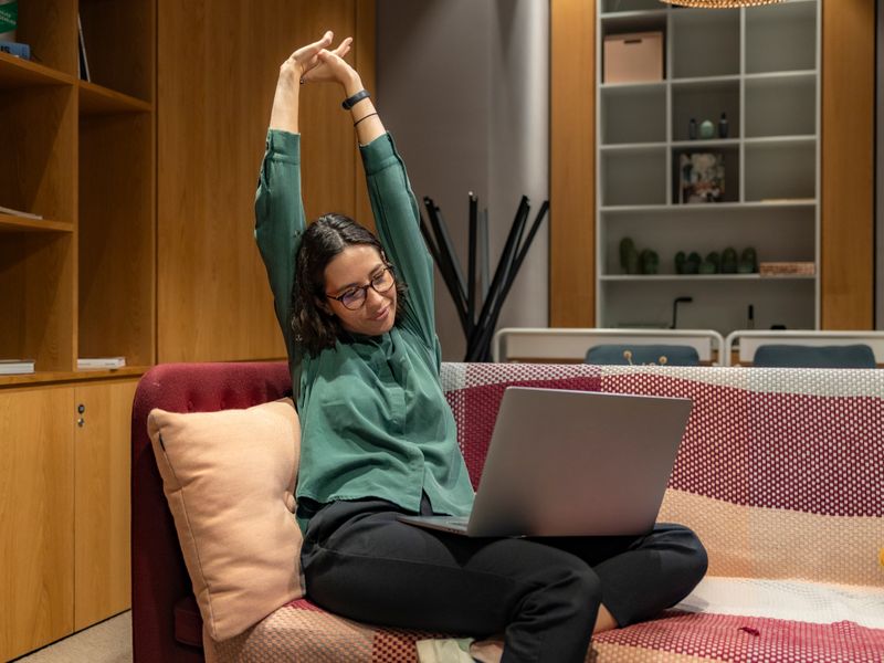 A woman relaxes while working from home on a sofa, showcasing a flexible work environment.