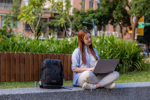 Young woman using laptop outdoors in a park, embracing flexible work lifestyle.