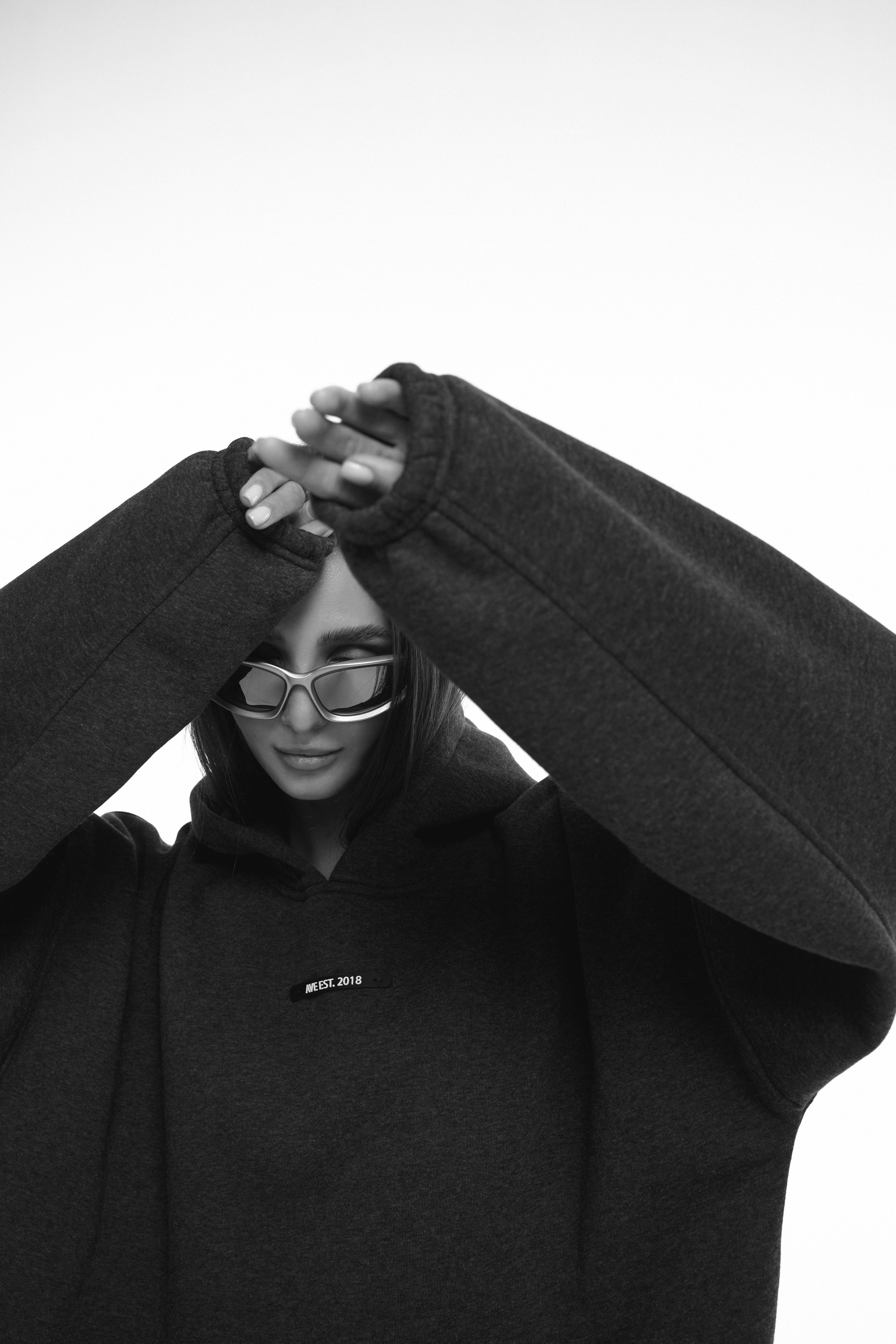 Chic portrait of a woman in a large black hoodie and stylish sunglasses, posing elegantly.