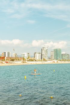 A person paddleboarding on a sunny day in Barcelona with city skyline backdrop.