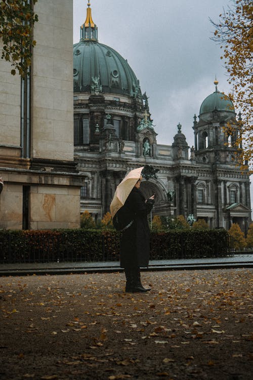 Woman with Umbrella Standing on Pavement with Ornamented Building behind