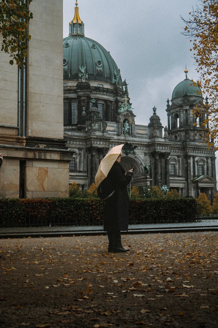 Woman With Umbrella Standing On Pavement With Ornamented Building Behind