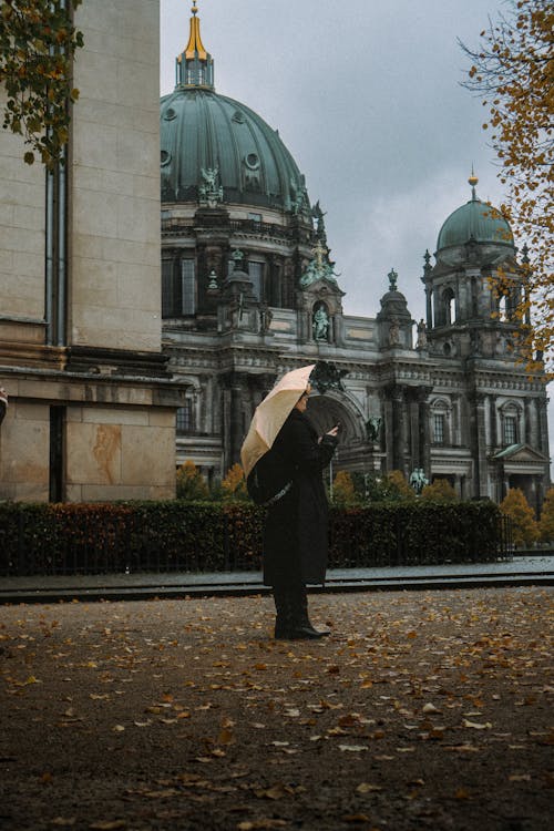 Free Woman with Umbrella Standing on Pavement with Ornamented Building behind Stock Photo