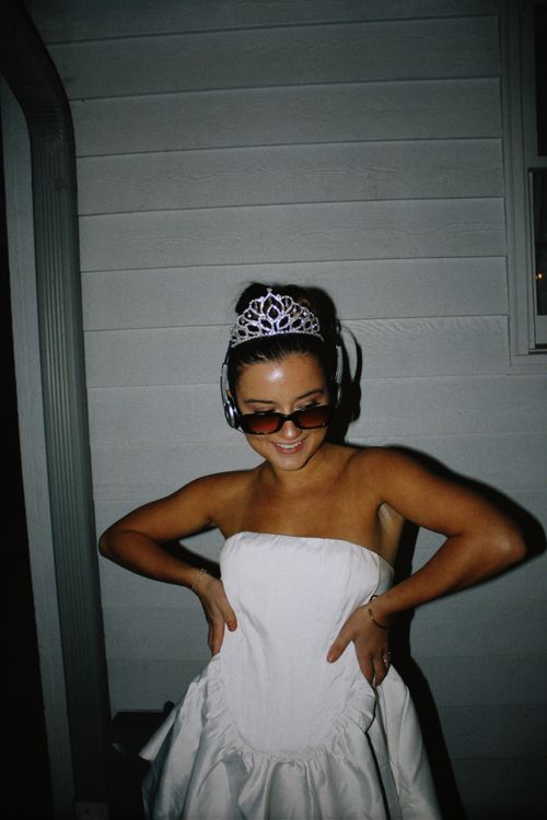 Free Fashionable woman in a white dress and tiara poses with confidence under night lights. Stock Photo