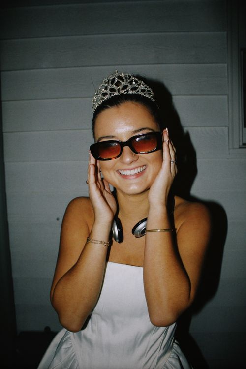Free Woman in a tiara and sunglasses smiling, enjoying nighttime festivities. Stock Photo